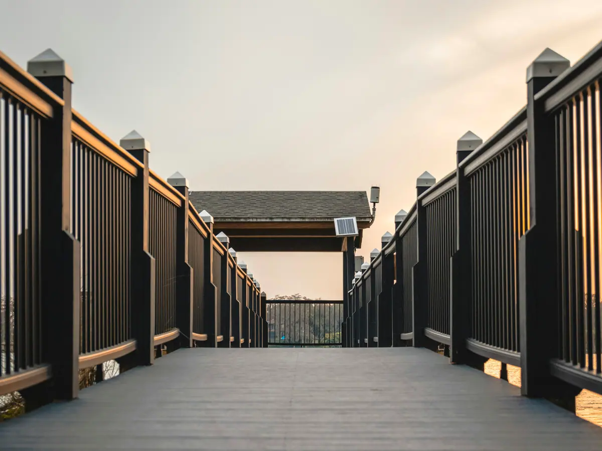 Narrow composite walkway deck with black railings and lit posts