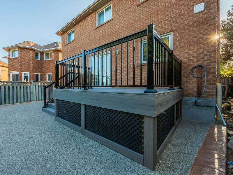 Raised dark deck with black aluminum railing and stairs beside a brick house