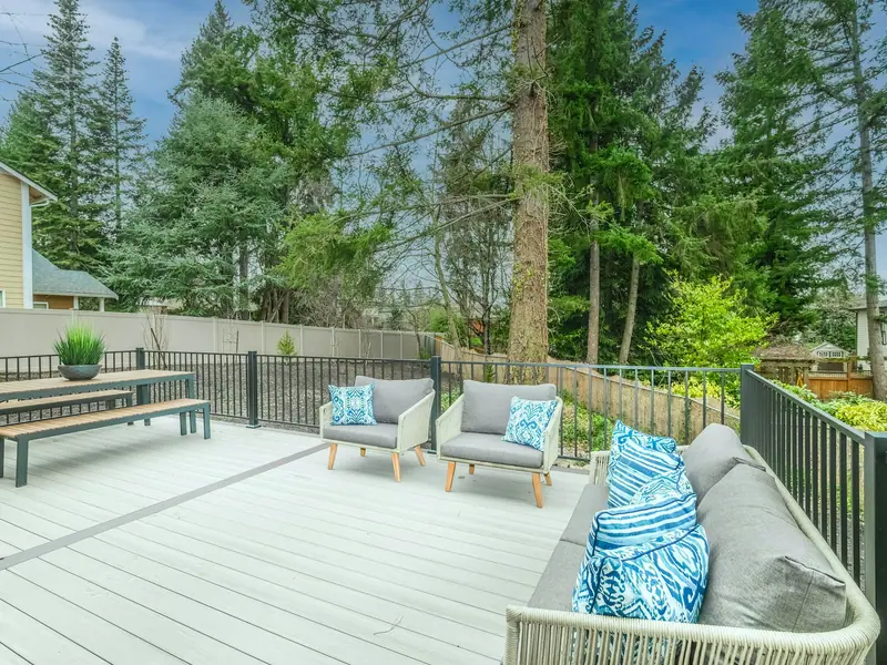 Light grey PVC deck with a white bench, lounge chairs and cushions in a treed backyard