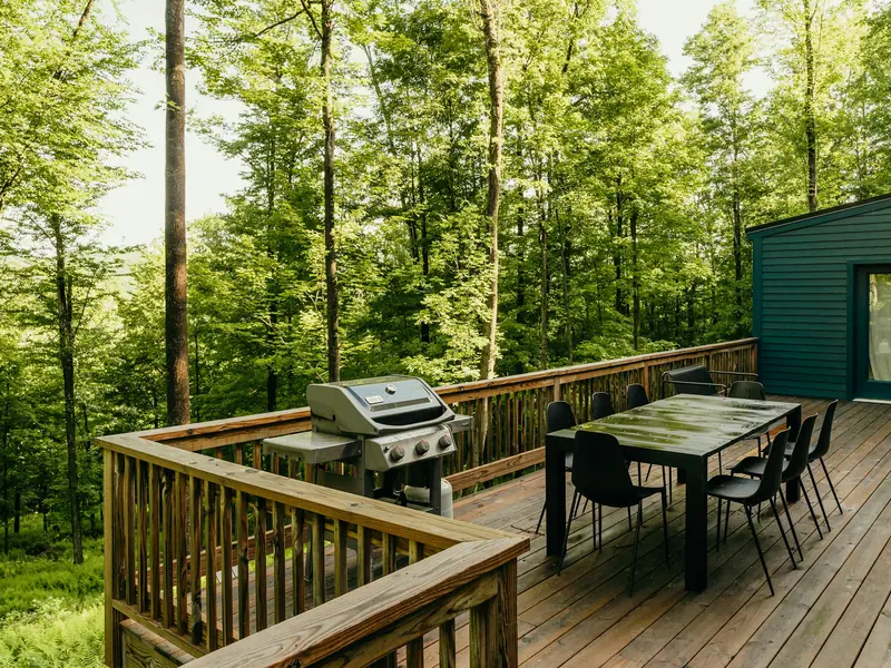 Cedar deck in a wooded backyard with a dining table and barbecue